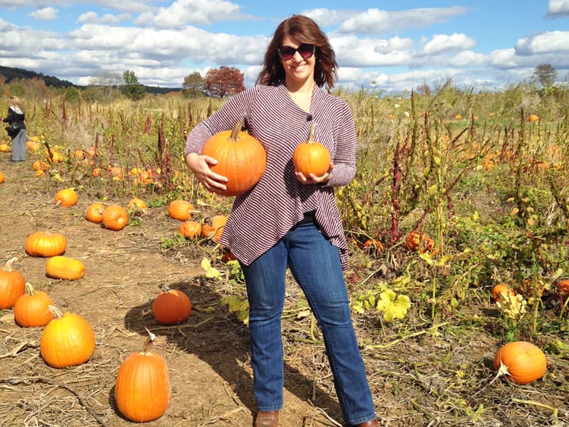 Woman holding two pumpkings in a pumpkin field.