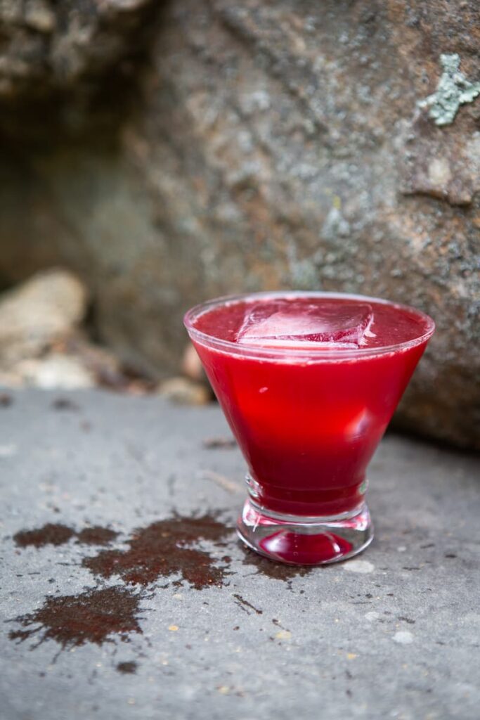 Red cocktail on a rock with spills next to it.