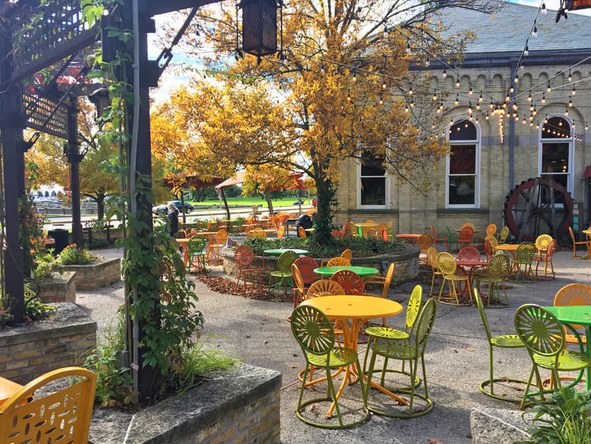 Patio with red, orange and yellow tables and chairs and trees and flowers.