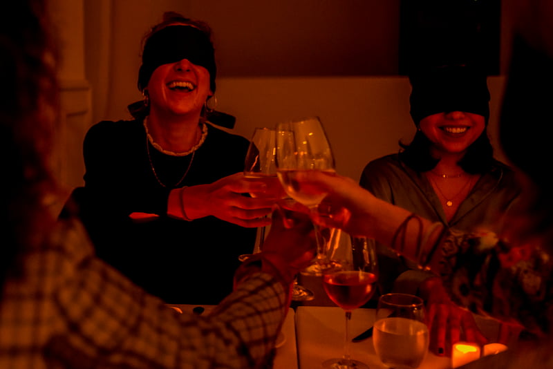 Blindfolded women toasting with wine glasses.