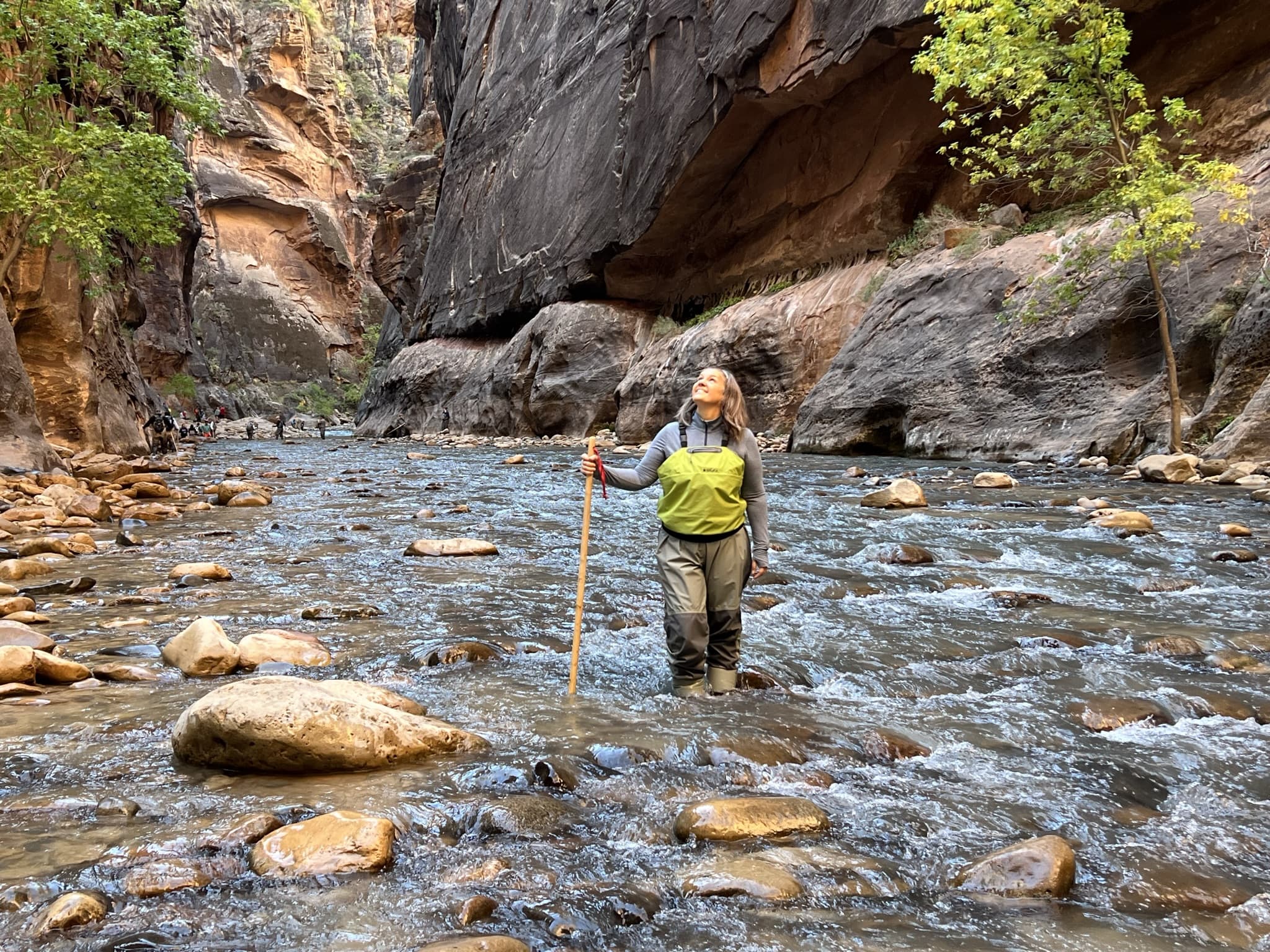 Woman in green vest walking in river with rock formations in background