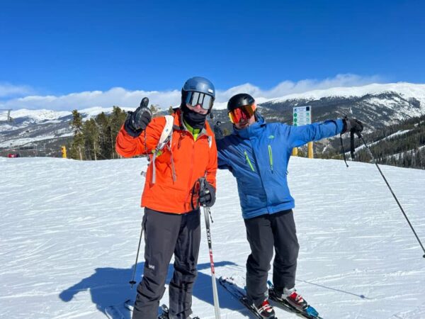 Two men standing on ski slope giving the thumbs up.